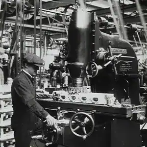 Industrial worker operating vintage manufacturing equipment in a historic factory setting.