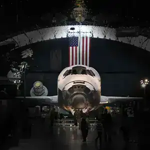 Space Shuttle Discovery displayed in a hangar with an American flag backdrop, showcasing historic sp.